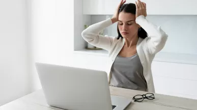 Mujer tomándose la cabeza mientras trabaja en la laptop representando el sindrome burnout