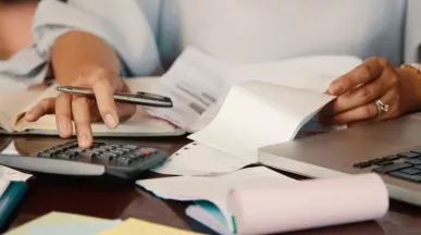 Persona revisando cuentas y documentos para consultar la devolución del IRPF en Uruguay desde una computadora portátil.
