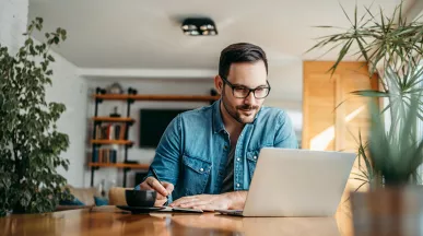 Hombre trabajando con una computadora portátil y tomando notas para planificar una estrategia de beneficios laborales en Uruguay.