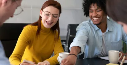 Cuatro personas en la oficina trabajando en conjunto mientras ríen y comparten un café
