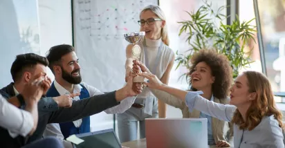 Colaboradores celebran un reconocimiento laboral levantando un trofeo en equipo durante una reunión.