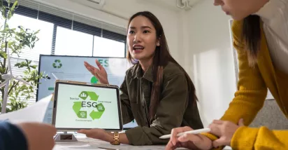 Profesional presentando una propuesta de ESG a su equipo, mostrando en una tablet los pilares de sostenibilidad ambiental, social y de gobernanza durante una reunión de trabajo.